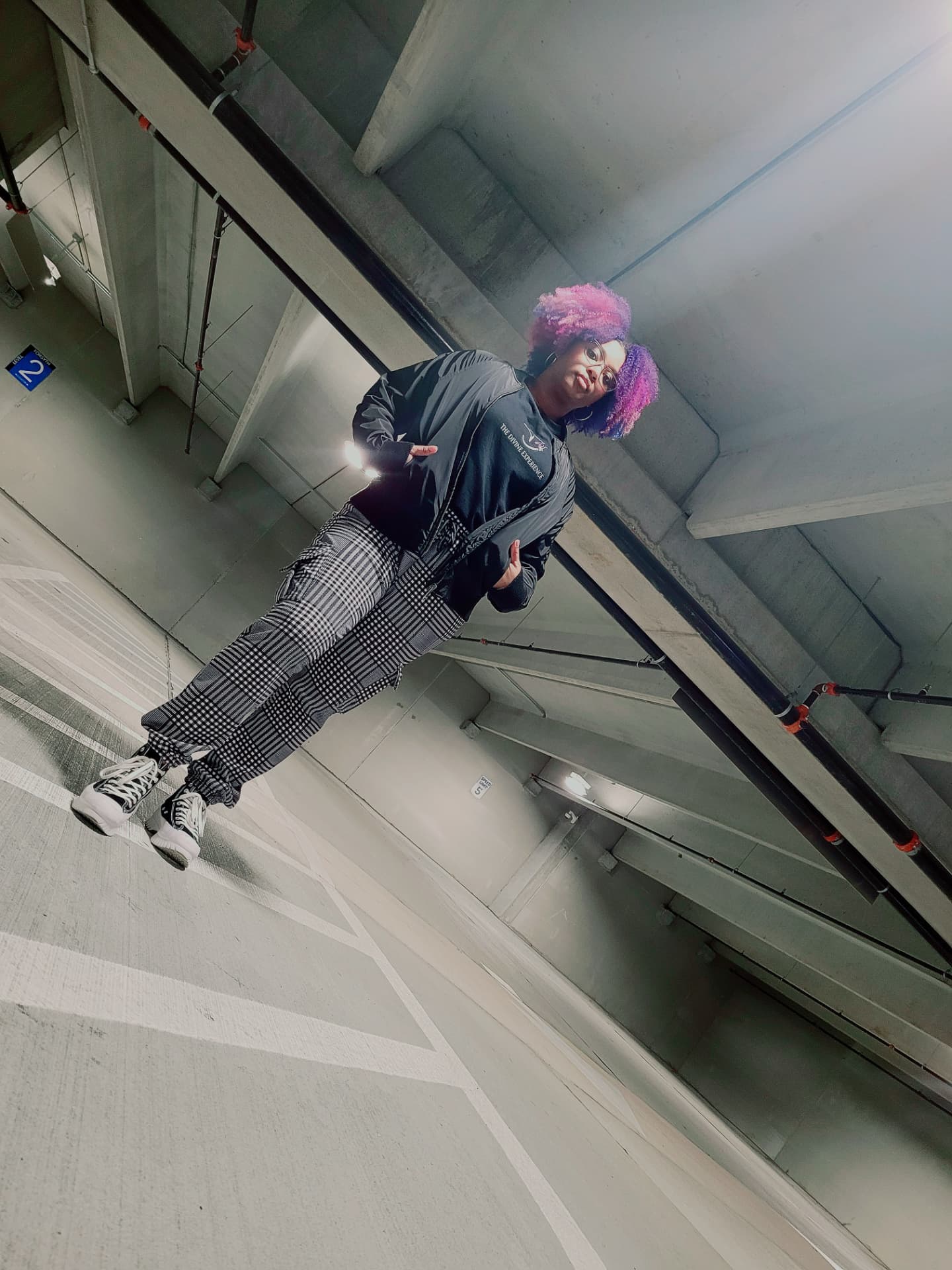 Quante' in a bomber jacket and plaid pants in a parking garage