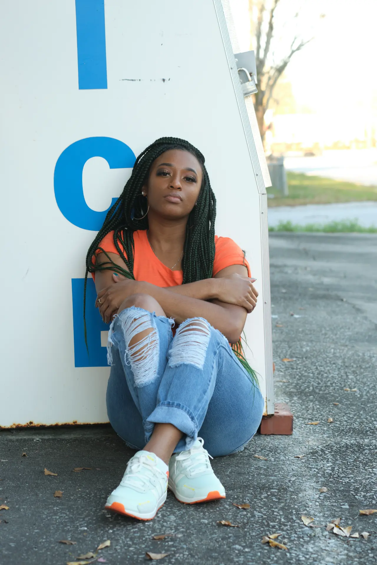 Quante' sitting against a painted ice sign in an orange tee and ripped jeans